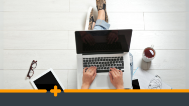 Widok z góry na zorganizowane stanowisko pracy osoby pracującej na laptopie, otoczoną kawą, tabletem, kawa i słuchawkami na jasnej podłodze